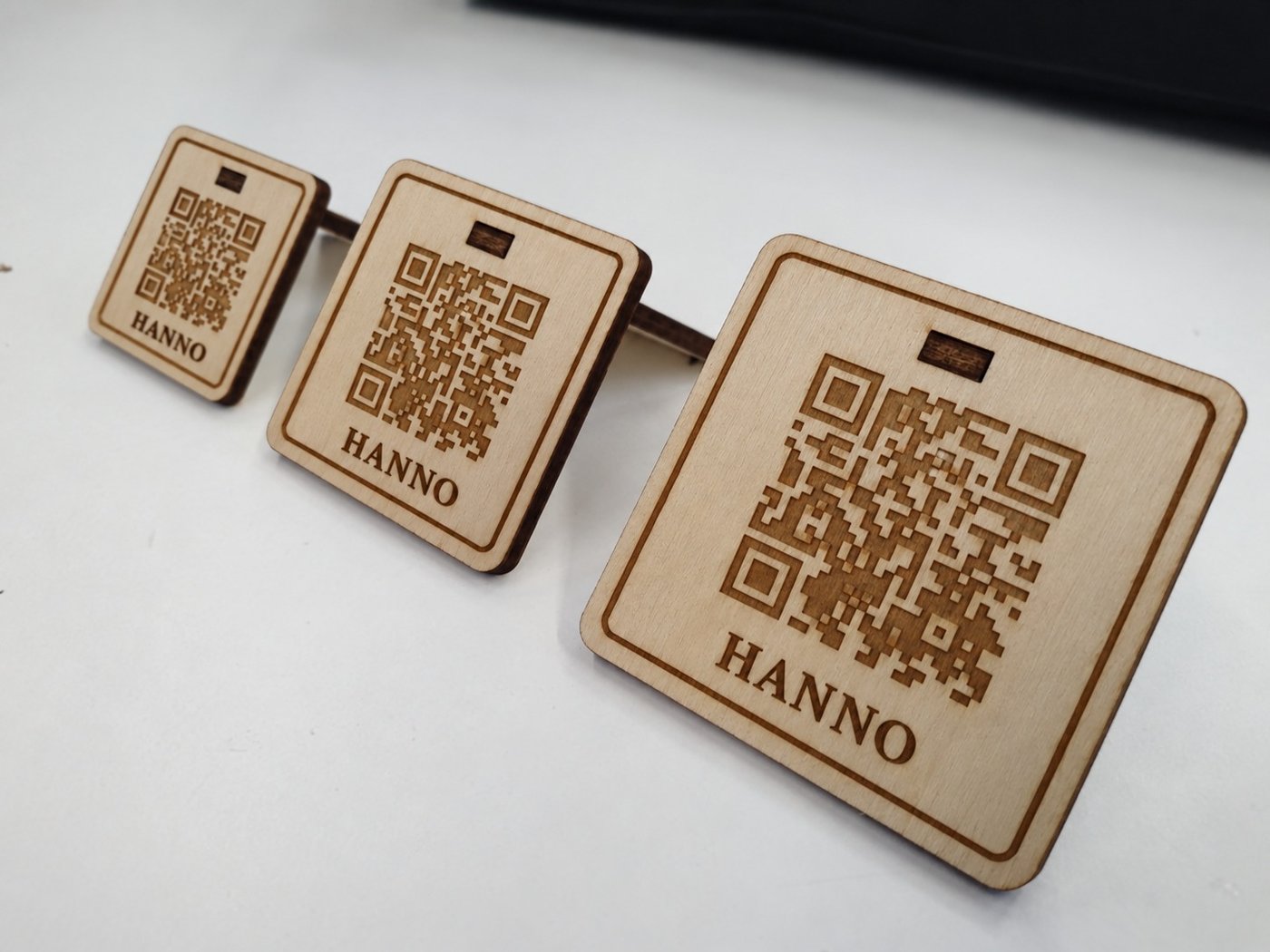 Three co:carte QR stands in wood, each engraved with a name and a QR code, in increasing size