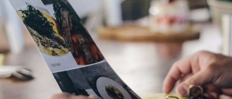 Een glanzend geplastificeerd fotomenu dat aan een restauranttafel wordt opengehouden
